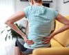 woman sat on sofa holding lower back in pain.