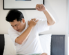 Man in white t-shirt holding left arm in the air. Right arm is touch the left shoulder in pain.