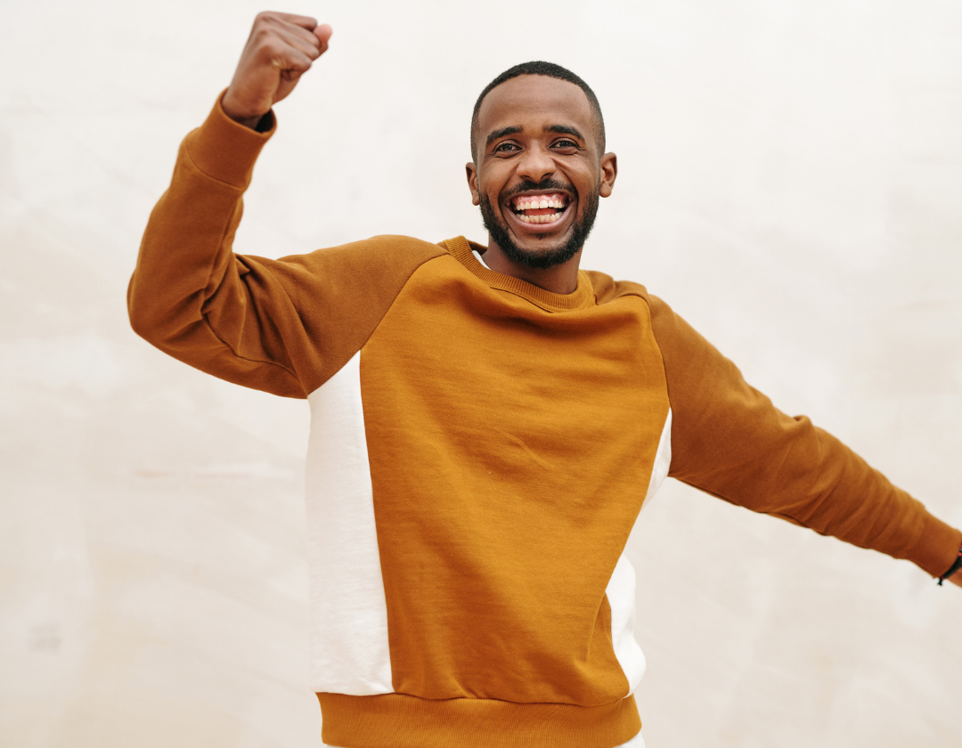 Man in orange sweatshirt cheering with arm in the air.
