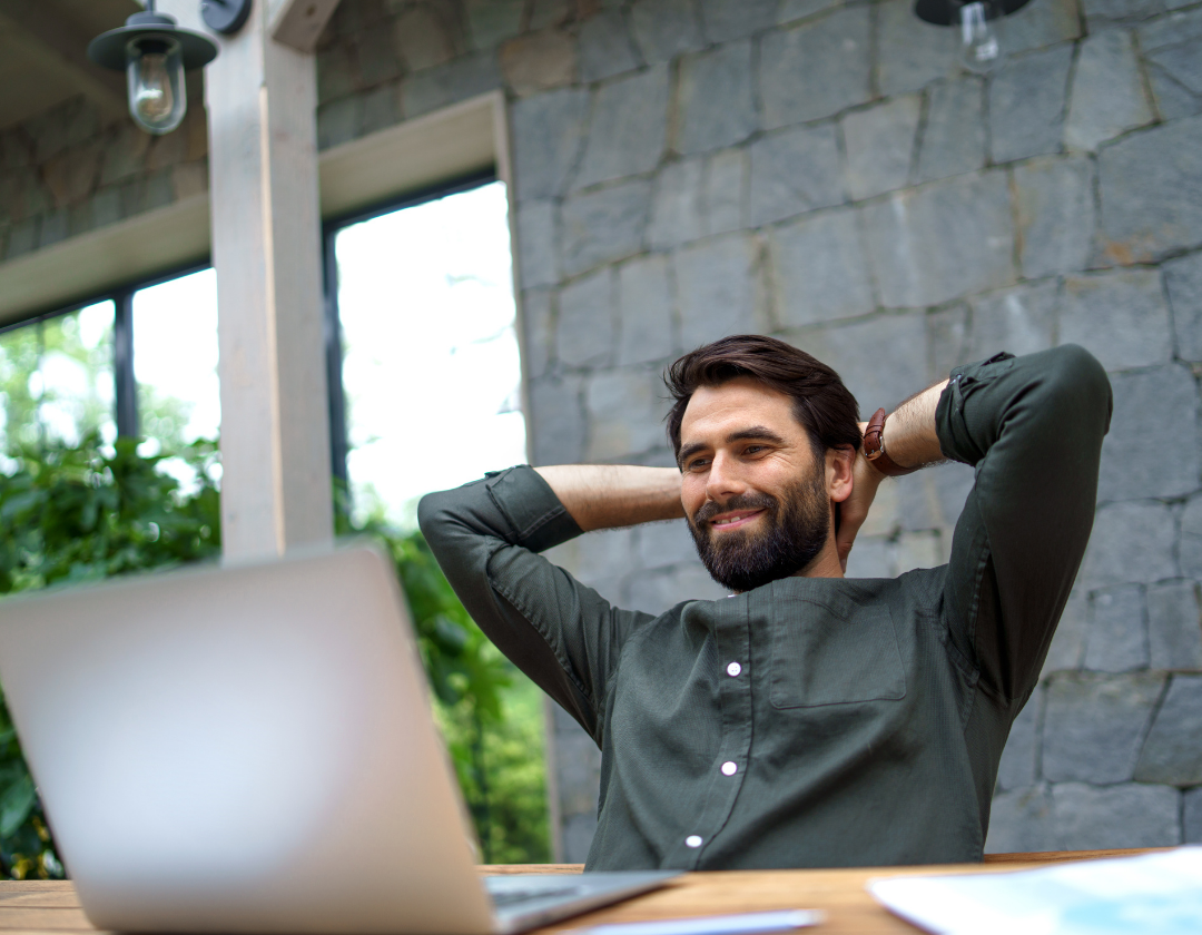 Man with hands behind his head smiling at laptop.
