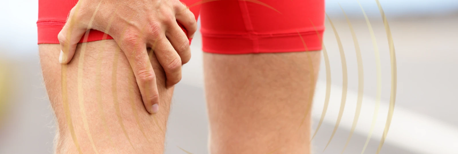 Man in red shorts close up of him holding his upper leg in pain.