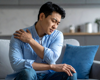 Man in blue sitting down holding shoulder in pain.