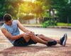 Man in activewear sitting on the flooring holding his knee in pain