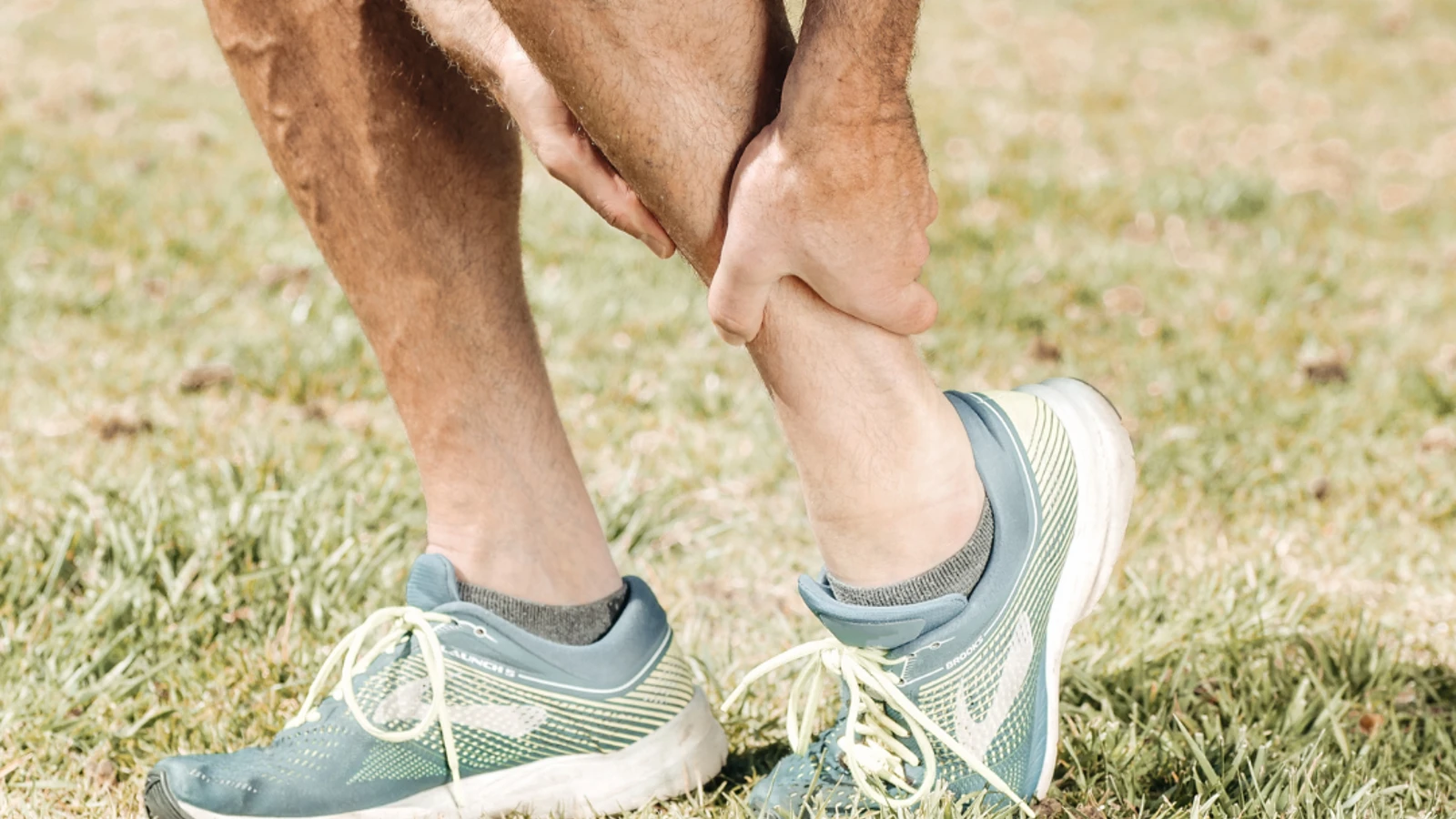 Close up of man in running trainers holding his ancle in pain.