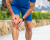 Man in blue running gear holding knee in pain.