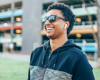 Man in zip up hoodie smiling with sunglasses and airpods.
