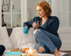 Woman sitting with cup of tea on sofa.