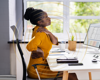 Woman in orange dress sat at a desk with upper back pain.