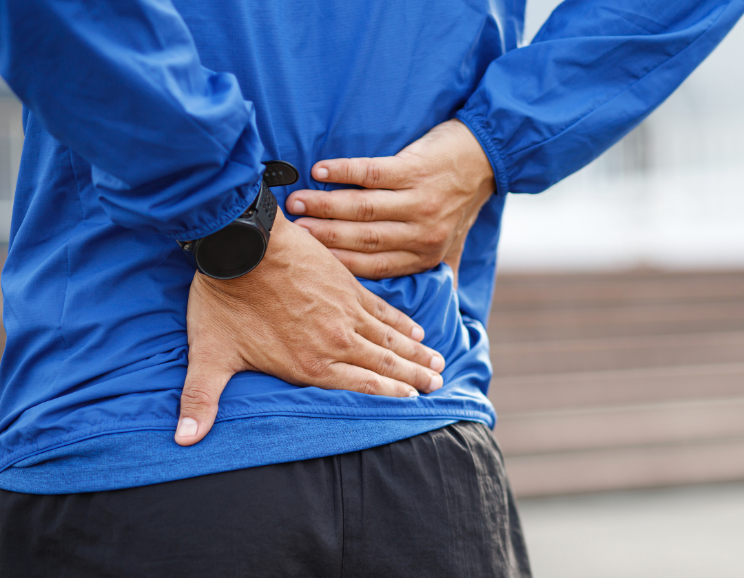 Young man in blue long sleeve running top holding lower back in pain.