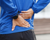 Young man in blue long sleeve running top holding lower back in pain.