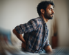 Man sat on bed with back pain.