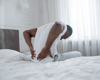 Man sat on bed facing away from camera holding lower back in pain.